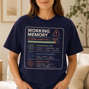 May include: A navy blue short-sleeve t-shirt featuring a graphic design that mimics a computer system interface. The text reads WORKING MEMORY, STORAGE ALMOST FULL, 92%, RESPONSIBILITIES, PEOPLE & MESSAGES, and MENTAL LOAD with various icons.