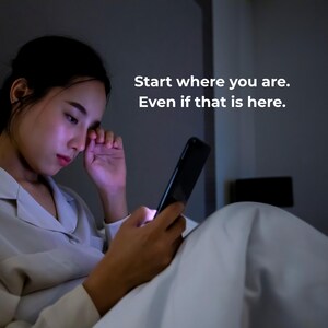 A person in bed in a dimly lit room looks at a smartphone, with text overlay: "Start where you are. Even if that is here."