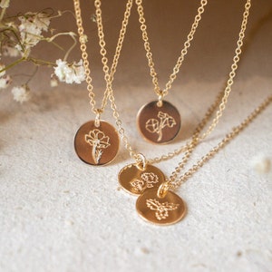 May include: Three gold necklaces with delicate chains and round pendants featuring engraved floral designs. The pendants are layered and the necklaces are displayed against a white background.