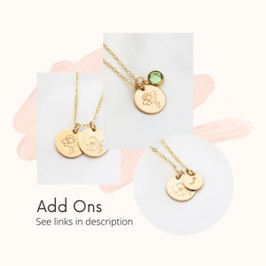May include: Gold necklace with two small round charms featuring engraved flower designs. The necklace also has a small green gemstone charm.