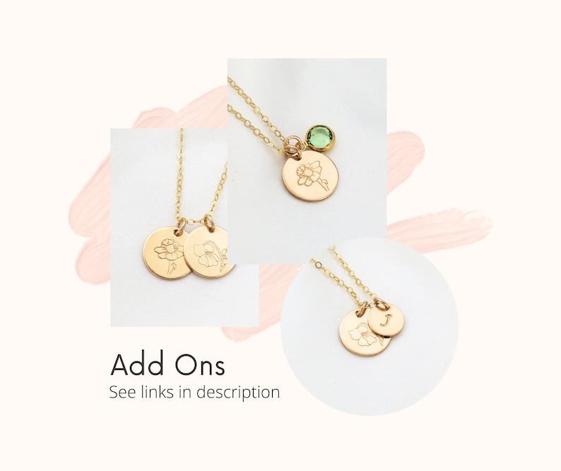 May include: Gold necklace with two small round charms featuring engraved flower designs. The necklace also has a small green gemstone charm.