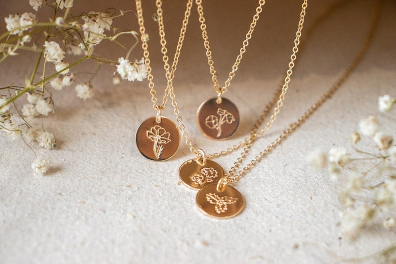 May include: Three gold necklaces with delicate chains and round pendants featuring engraved floral designs. The pendants are layered and the necklaces are displayed against a white background.