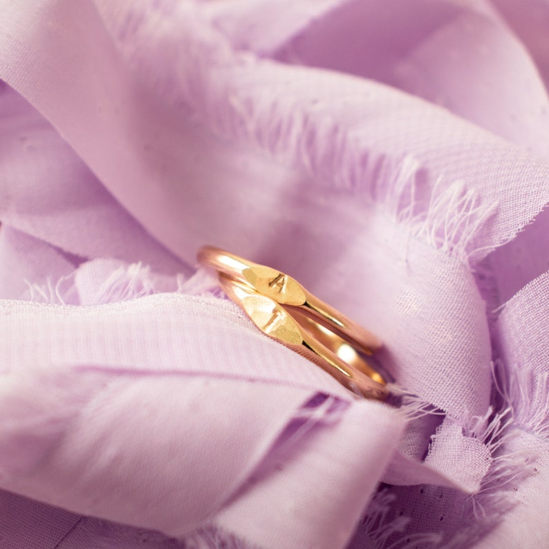 K&ouml;nnte beinhalten: Zwei goldene Ringe, die &uuml;bereinander liegen, der obere Ring hat eine kleine dreieckige Form an der Seite. Die Ringe liegen auf einem weichen, violetten Stoff.