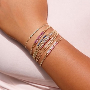 May include: A set of six delicate gold chain bracelets, each featuring a small segment of tiny, multi-coloured gemstone beads. The bracelets include beads in shades of light green, pink, blue, and white, arranged in a simple, refined design.
