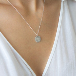 May include: A silver chain necklace with a small, round pendant featuring a delicate floral design.