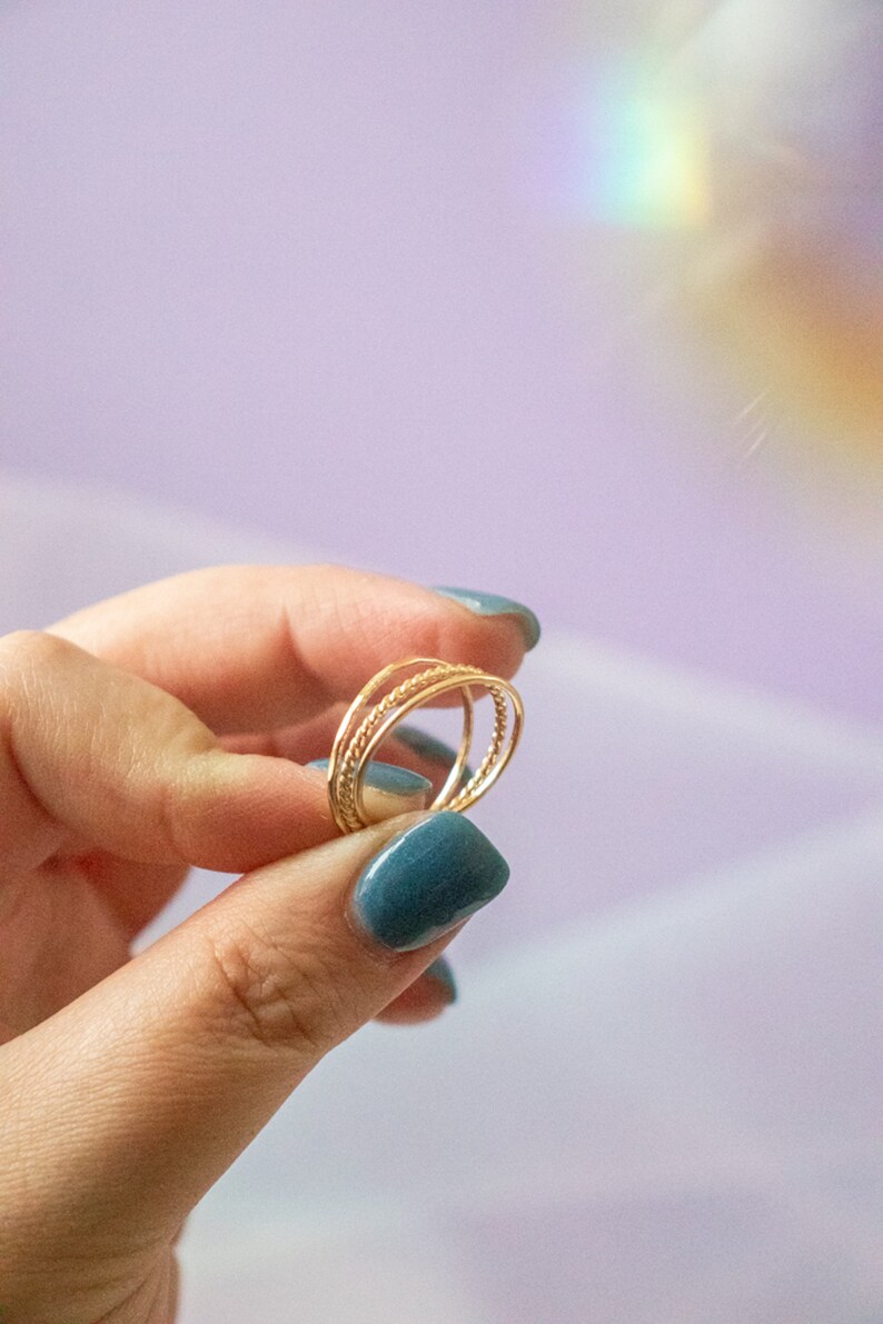 Puede incluir: Un conjunto de tres anillos finos de oro apilados en un dedo. Los anillos est&aacute;n hechos de alambre trenzado y tienen un dise&ntilde;o delicado y minimalista.