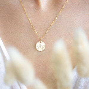 May include: A gold chain necklace with a delicate flower pendant. The pendant is a small, round disc with a floral design.
