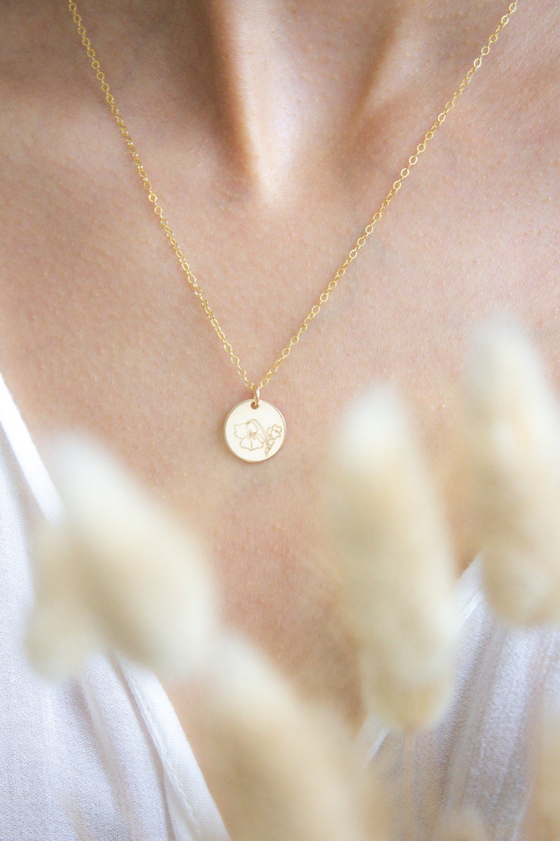 May include: A gold chain necklace with a delicate flower pendant. The pendant is a small, round disc with a floral design.