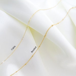 May include: Two gold chains on a white background. The chain on the left is a cable chain, and the chain on the right is a beaded chain. The text "Cable" is written below the cable chain, and the text "Beaded" is written below the beaded chain.