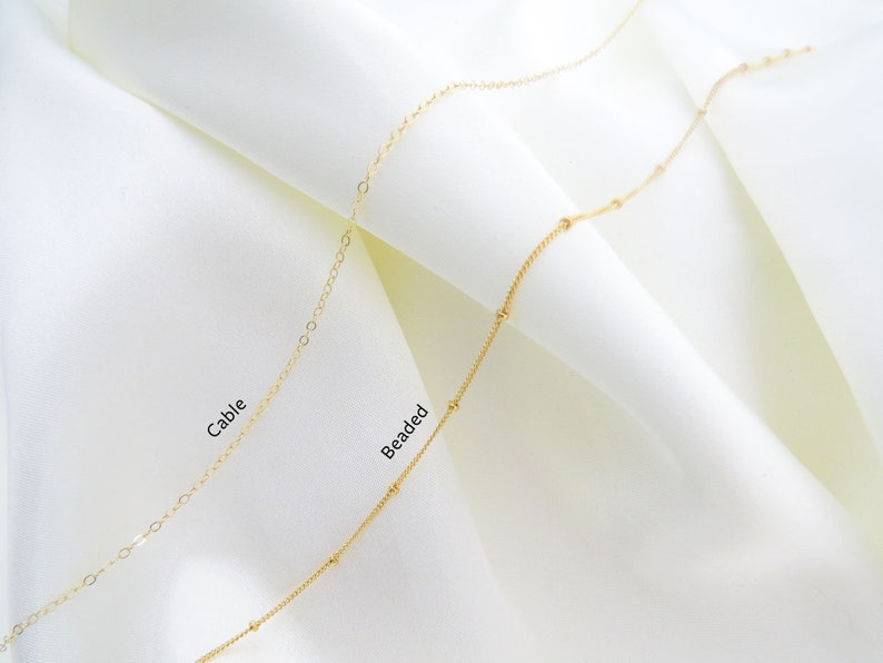 May include: Two gold chains on a white background. The chain on the left is a cable chain, and the chain on the right is a beaded chain. The text "Cable" is written below the cable chain, and the text "Beaded" is written below the beaded chain.