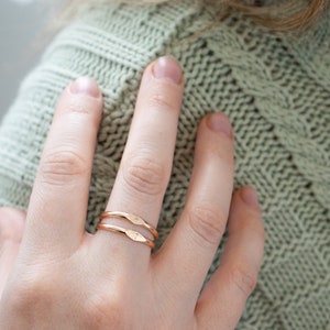 K&ouml;nnte beinhalten: Zwei d&uuml;nne goldene Ringe, die auf einem Finger &uuml;bereinander liegen. Die Ringe sind schlicht und haben eine leicht geh&auml;mmerte Textur.