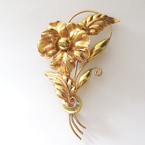 May include: A gold-toned flower brooch with a large central flower and smaller leaves. The brooch has a delicate, intricate design.