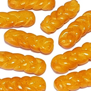 May include: An overhead shot displays several golden-brown, braided pastries against a white background. The baked goods have a glossy sheen, suggesting a glaze. The arrangement of the pastries varies, with some oriented horizontally and others diagonally.