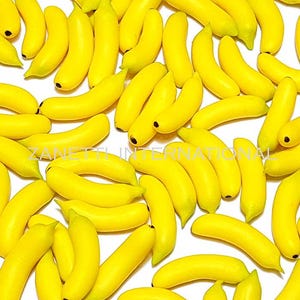 Puede incluir: Una colección de plátanos artificiales de color amarillo brillante. Cada plátano tiene una forma curva con una punta oscura. Los plátanos están dispersos por la imagen, creando una disposición visualmente atractiva. El texto "ZANETTI INTERNATIONAL" es visible.
