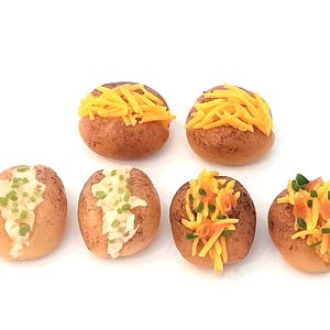 Könnte beinhalten: Sechs Miniatur-Ofenkartoffeln, jede mit einem anderen Belag. Zwei sind mit geriebenem Cheddar-Käse belegt, zwei mit einer cremigen weißen Sauce und grünen Schnittlauch, und zwei mit einer Mischung aus Käse, Schnittlauch und orangener Garnitur.