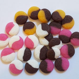 Peut inclure: Un assortiment de biscuits ronds colorés. Certains sont divisés en blanc et rose, d'autres en blanc et marron foncé, et d'autres en jaune et marron foncé. Les biscuits sont disposés sur une surface blanche.