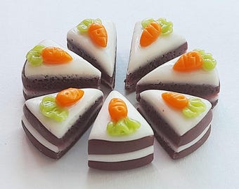 Peut inclure: Sept petites parts de gâteau aux carottes disposées en cercle. Chaque part a une base marron foncé, un glaçage blanc et est surmontée d'une carotte orange et de feuilles vertes. Les gâteaux sont sur une surface blanche.