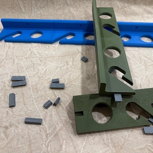 May include: A blue and green 3D-printed tool with multiple holes and slots, along with several small gray rectangular pieces. The tool appears to be designed for a specific purpose, possibly for organizing or holding items.