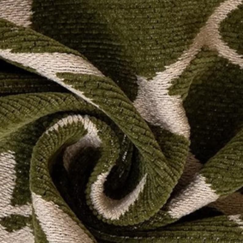 May include: Close-up of a folded fabric with a textured, geometric pattern. The fabric features a deep olive green color with a contrasting off-white design. The material appears soft and plush, with a subtle sheen.
