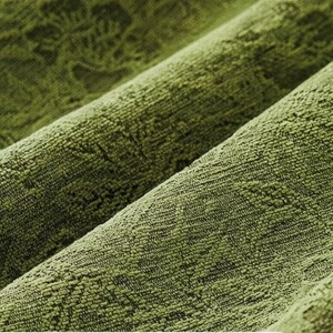 May include: Close-up of a textured, olive green fabric with a subtle, repeating pattern. The fabric is folded in diagonal lines, creating shadows and highlighting the texture. The material appears soft and plush.