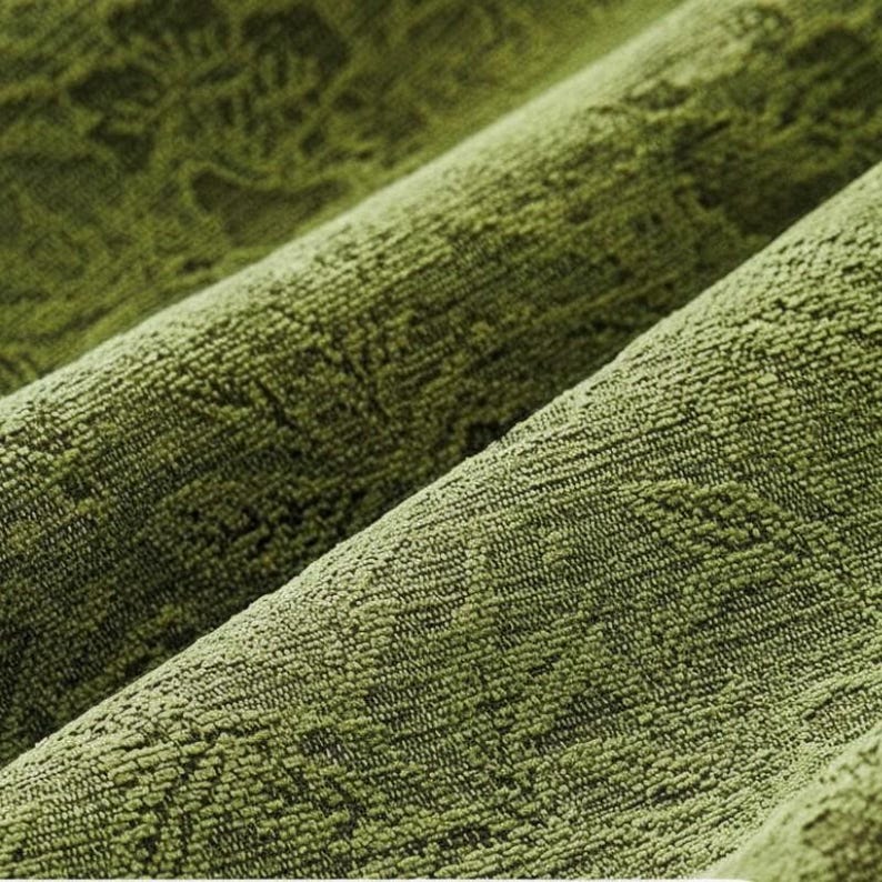 May include: Close-up of a textured, olive green fabric with a subtle, repeating pattern. The fabric is folded in diagonal lines, creating shadows and highlighting the texture. The material appears soft and plush.