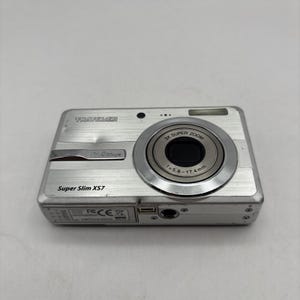 以下が含まれることがあります： シルバーのTraveler Super Slim XS7デジタルカメラ。3倍ズームレンズを搭載し、焦点距離は5.8〜17.4mmです。カメラは9.0メガピクセルの解像度とコンパクトなデザインです。カメラにはフラッシュと小さな画面があります。