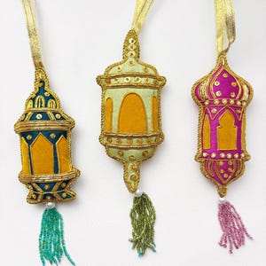 May include: Three decorative hanging lanterns with beaded tassels. The lanterns are made of fabric and embroidered with gold thread. The lanterns are in the colors of teal, green, and pink.