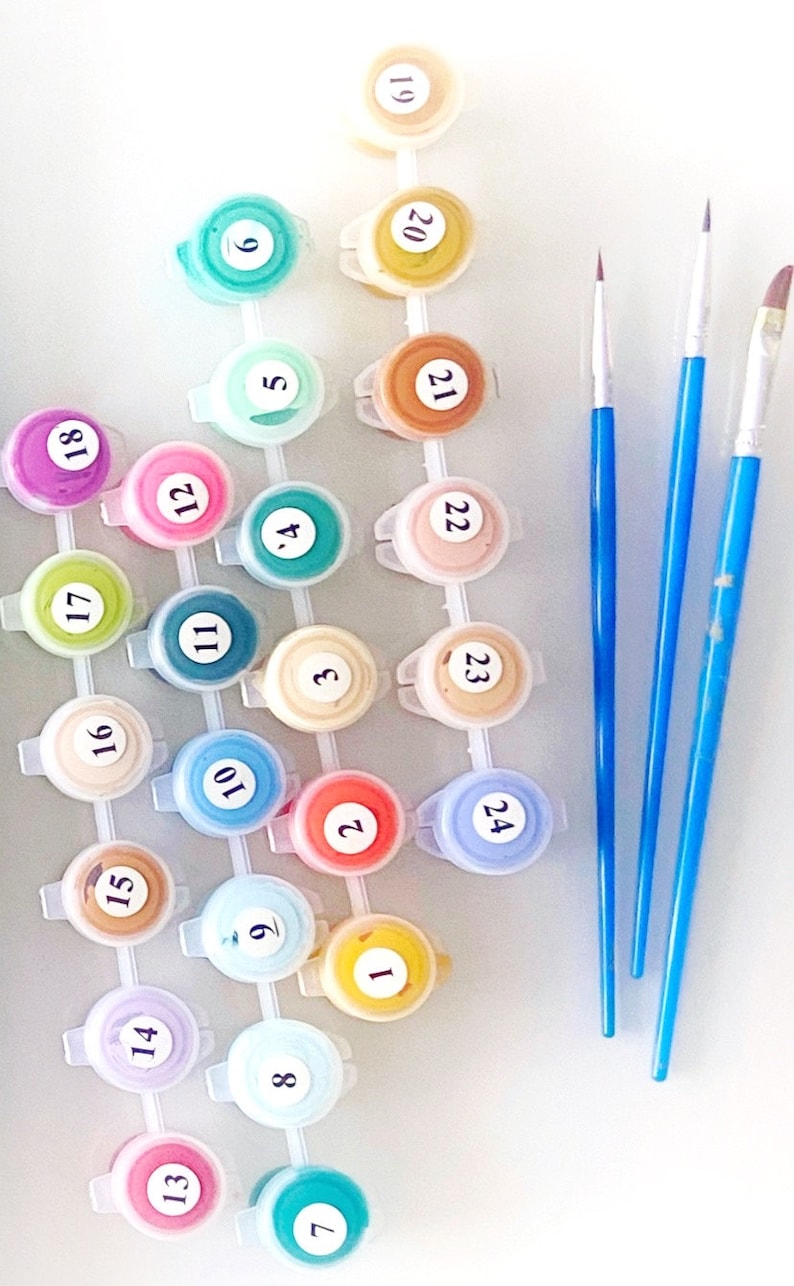 May include: A paint-by-numbers kit with numbered paint pots in various colors, arranged in a grid. Three blue-handled paintbrushes are positioned to the right. The paint pots are labeled with numbers from 1 to 24.