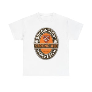 May include: White t-shirt featuring a vintage-style Boddingtons Strong Ale logo. The logo is oval-shaped with text that reads "Boddingtons", "Strong Ale", and "Manchester Brewery". The logo is in shades of brown, orange, and white.
