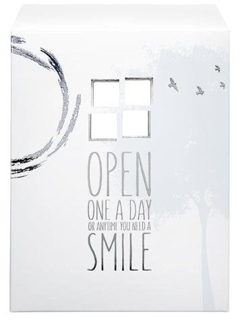 Op de afbeelding: Witte doos met een zilveren ontwerp en de tekst "OPEN ONE A DAY OR ANYTIME YOU NEED A SMILE".