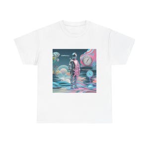 May include: White t-shirt featuring a colorful graphic print. The design includes a figure in a metallic suit, clocks, and the word "OMPHALI". The artwork has a surreal, dreamlike quality with pastel colors.