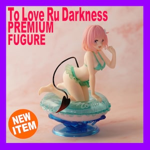 Könnte beinhalten: Premium-Figur aus "To Love Ru Darkness" mit einer Figur mit rosa Haaren und einem türkisfarbenen Bikini. Die Figur kniet auf einem blau-weißen Schwimmer mit einem schwarzen Schwanz. Der Text "NEW ITEM" befindet sich auf einem orangefarbenen Aufkleber.