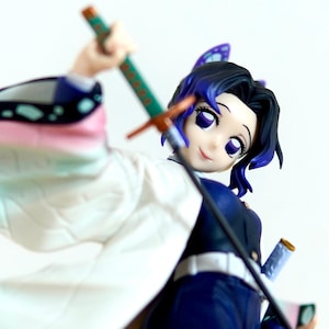 Könnte beinhalten: Anime-Figur eines weiblichen Charakters mit schwarzen und blauen Haaren, lila Augen und einem weißen und blauen Outfit. Sie hält ein Katana mit grünem Griff und orangefarbenen Akzenten. Die Figur hat eine dynamische Pose.