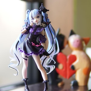Peut inclure: Figurine détaillée d'un personnage d'anime féminin avec de longs cheveux bleus et une robe noire et violette. La figurine a un ornement de tête décoratif et est posée dans une posture dynamique. Un petit personnage noir est perché sur son épaule.