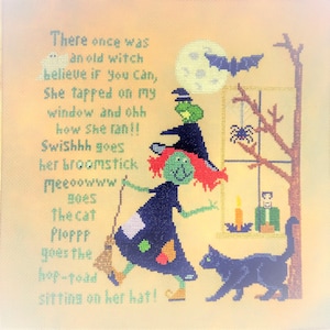 May include: A cross-stitch design depicting a green-skinned witch with red hair, wearing a black dress and hat, holding a broom. A black cat walks beside her. The design includes a full moon, a bat, and text.