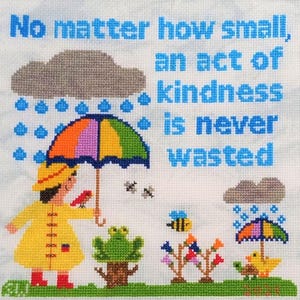 以下が含まれることがあります： 「No matter how small, an act of kindness is never wasted」の文字が入ったクロスステッチアート。黄色いレインコートと赤いブーツを履いた人が虹色の傘を持ち、鳥、カエル、蜂、花が描かれています。