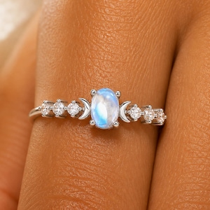 Peut inclure: Bague en argent ornée d'une pierre de lune ovale irisée. La bague est ornée de petites pierres rondes et transparentes et d'accents de croissant de lune. La bague est montée sur un fin anneau.