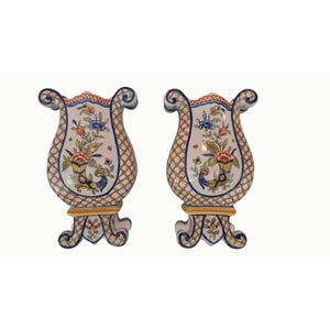 May include: A pair of matching ceramic vases featuring a cream-colored body with a brown lattice pattern. Each vase displays a central hand-painted floral motif in blue, red, green, and yellow, with ornate scroll-shaped handles and a flared base.