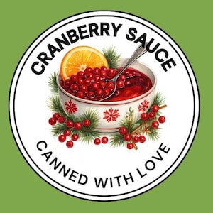Pode incluir: Um rótulo redondo sobre um fundo verde apresenta uma tigela de molho de cranberry com uma fatia de laranja e uma colher. A tigela é decorada com padrões florais vermelhos. O texto "CRANBERRY SAUCE CANNED WITH LOVE" é impresso na borda.