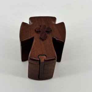 May include: A wooden cross-shaped box with a dark brown finish. The box features a carved cross on the top and a hinged opening. The design is simple and elegant, suitable for religious keepsakes or small items.