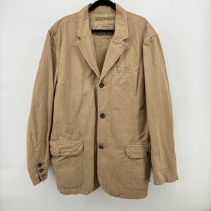May include: A tan blazer with a classic design. The jacket features a notched lapel, three buttons on the front, and two front pockets with flaps. The blazer is made of a durable fabric and has a relaxed fit.