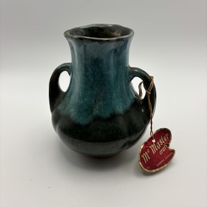 May include: A small, handcrafted ceramic vase with two handles. The vase has a dark teal and black glaze, with a tag that reads "McMaster craft Dundas Canada."