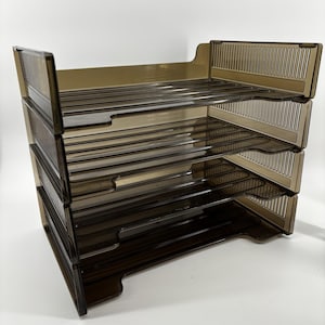 May include: A four-tier desk organizer made of translucent dark brown plastic. The unit features four stacked horizontal trays with open fronts and vertical slotted side panels, designed for sorting documents and office supplies on a flat surface.
