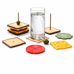 May include: A collection of sandwich-themed coasters and drink accessories. Includes a glass of water, a sandwich, a slice of cheese, a tomato, and a lettuce coaster. The sandwich has a toothpick with an olive.