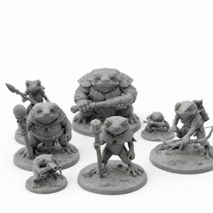 Pode incluir: Uma coleção de figuras de sapos cinzentos em várias poses, algumas segurando armas ou bastões. As figuras estão em bases circulares, com texturas e expressões detalhadas, sugerindo um tema de fantasia ou jogo de tabuleiro.