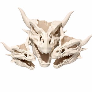 Three ivory dragon skull planters, one large and two smaller, arranged side by side with open jaws and curved horns on a white background.