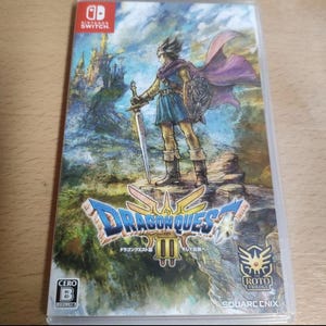 May include: A Nintendo Switch game case for Dragon Quest III. The cover art features a warrior with a sword and shield, standing on a rocky landscape. The game title is prominently displayed with Japanese text. The case is in a clear plastic sleeve.