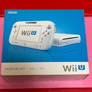 Puede incluir: Una consola y un mando blancos de Wii U Premium Set sobre una caja azul. El mando tiene el logotipo de Wii U y botones. La caja también muestra el logotipo de Wii U y el texto "32GB shiro". El logotipo de Nintendo está en la esquina superior izquierda.