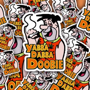 May include: A selection of stickers displaying a cartoon character with the words "Yabba Dabba Doobie." The character is in an orange top with a green collar and a cannabis leaf. The stickers have a white background and a black border.