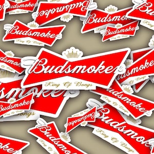 Peut inclure: Plusieurs autocollants rouges et blancs avec le texte "Budsmoke" dans une police stylisée, rappelant un logo de bière. L'expression "King Of Bongs" est également présente. Les autocollants sont dispersés sur un fond neutre.